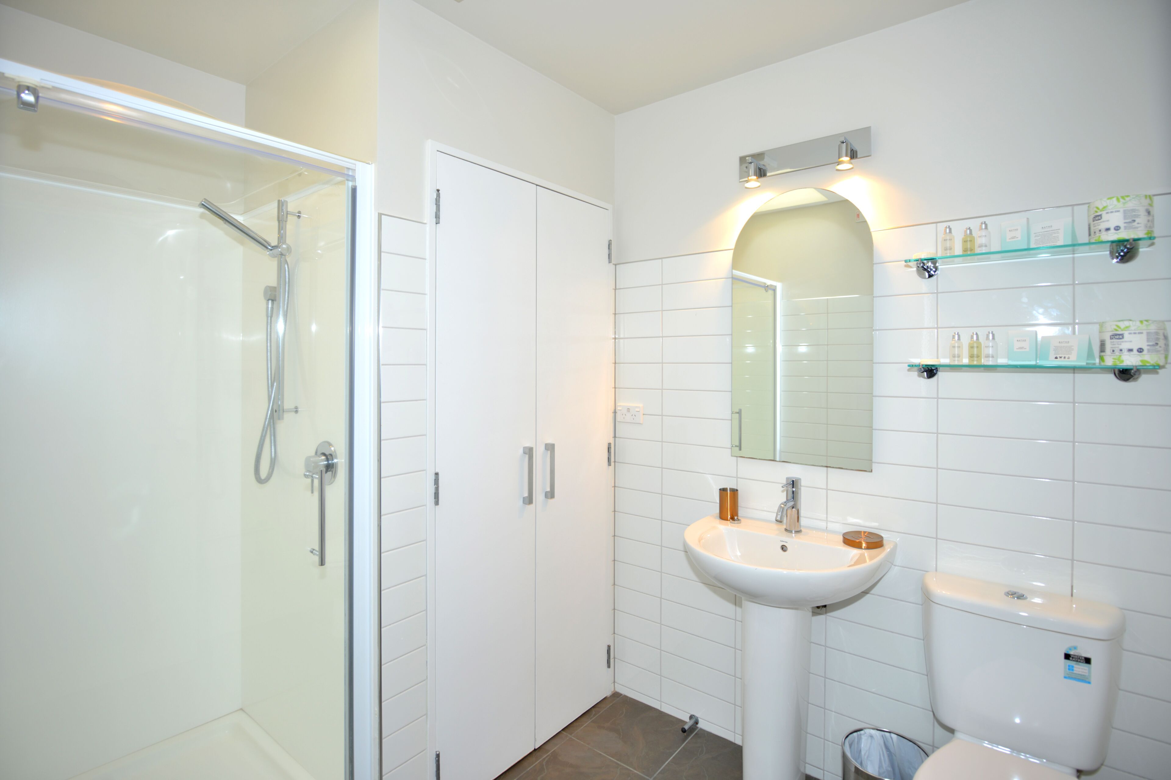 A modern bathroom with a glass-enclosed shower, a pedestal sink, and a toilet.