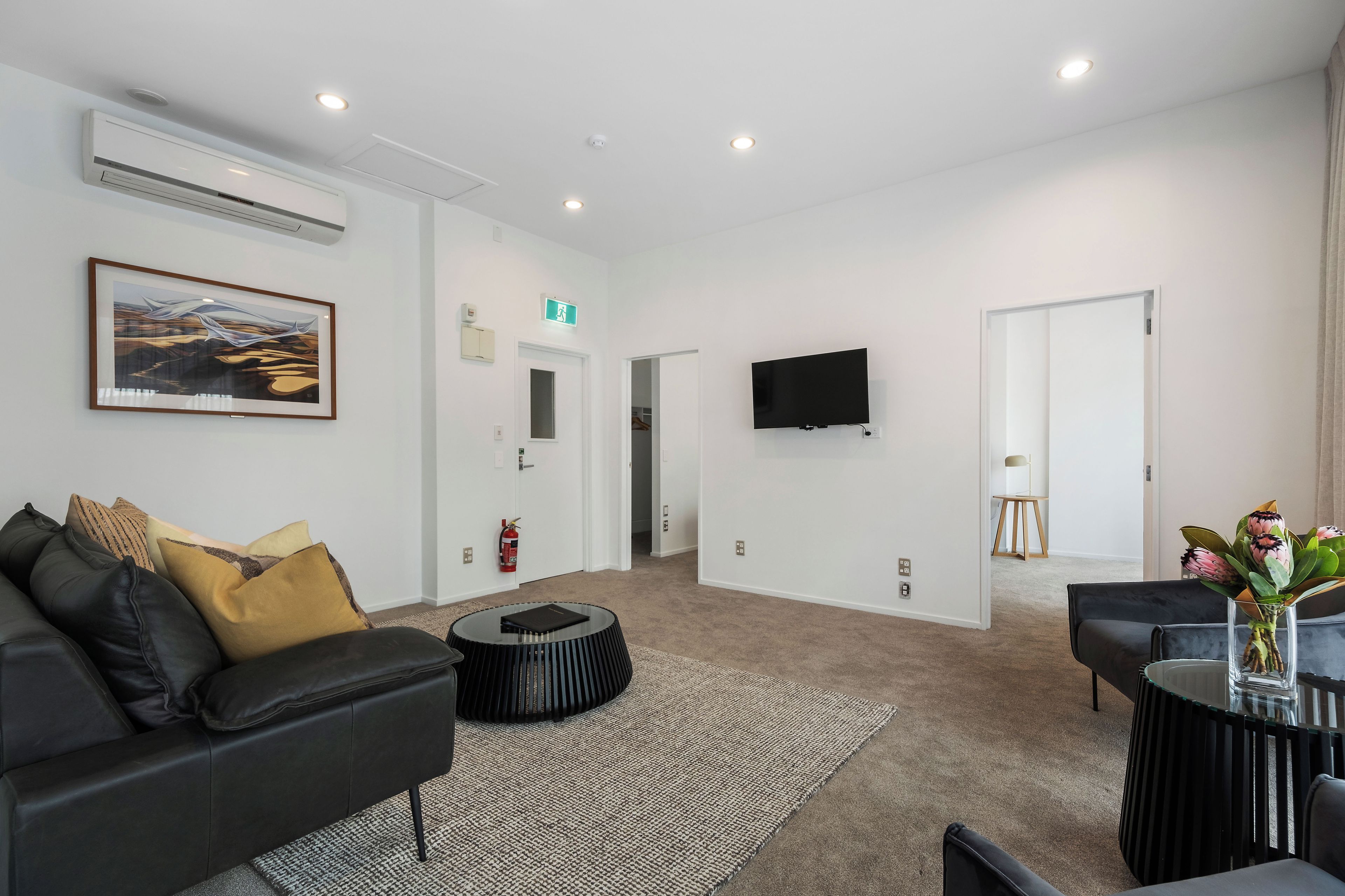 A modern living room with a black leather sofa, a round coffee table, a flat-screen TV mounted on the wall, and a framed painting on the wall.