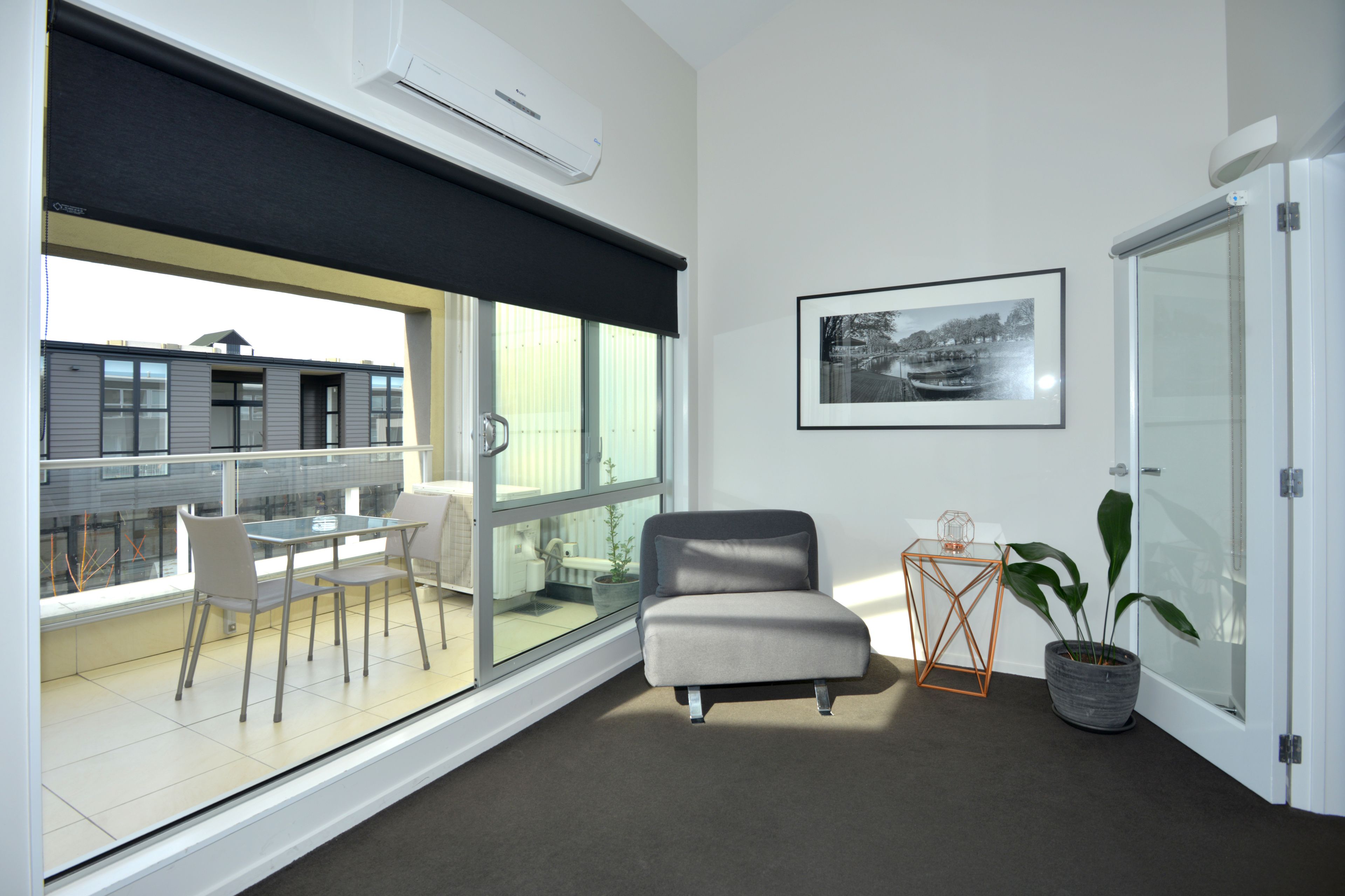 A modern living room with a large window, a grey sofa, a small table, and a potted plant.