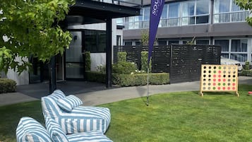 Un hotel moderno con fachada de vidrio, mobiliario exterior con cojines a rayas y una bandera que indica el nombre del hotel.