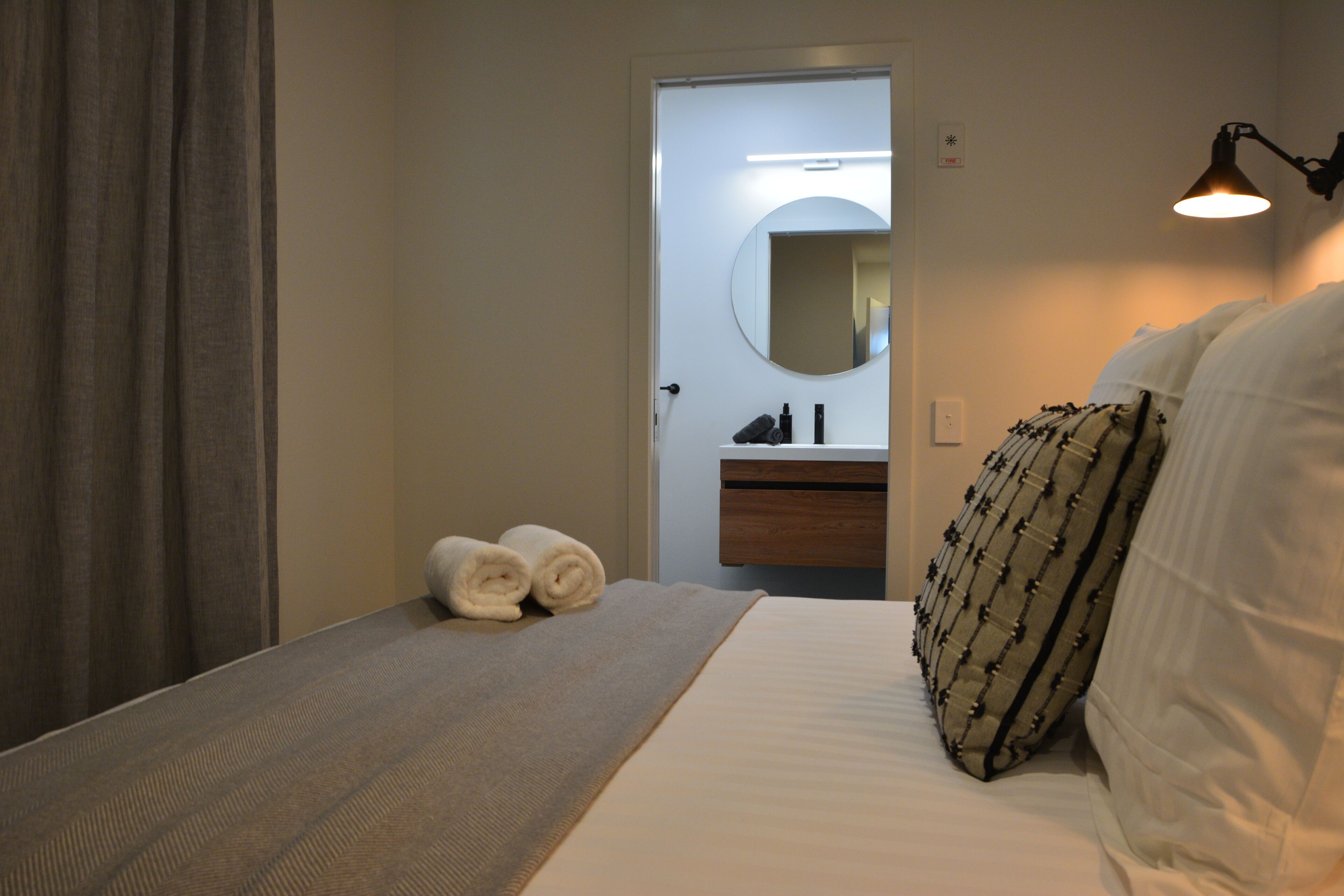 Una habitación de hotel con cama, mesita de noche, espejo y lámpara.