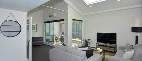 Ein modernes Wohnzimmer mit grauem Sofa, Flachbildfernseher und einem Oberlicht.
