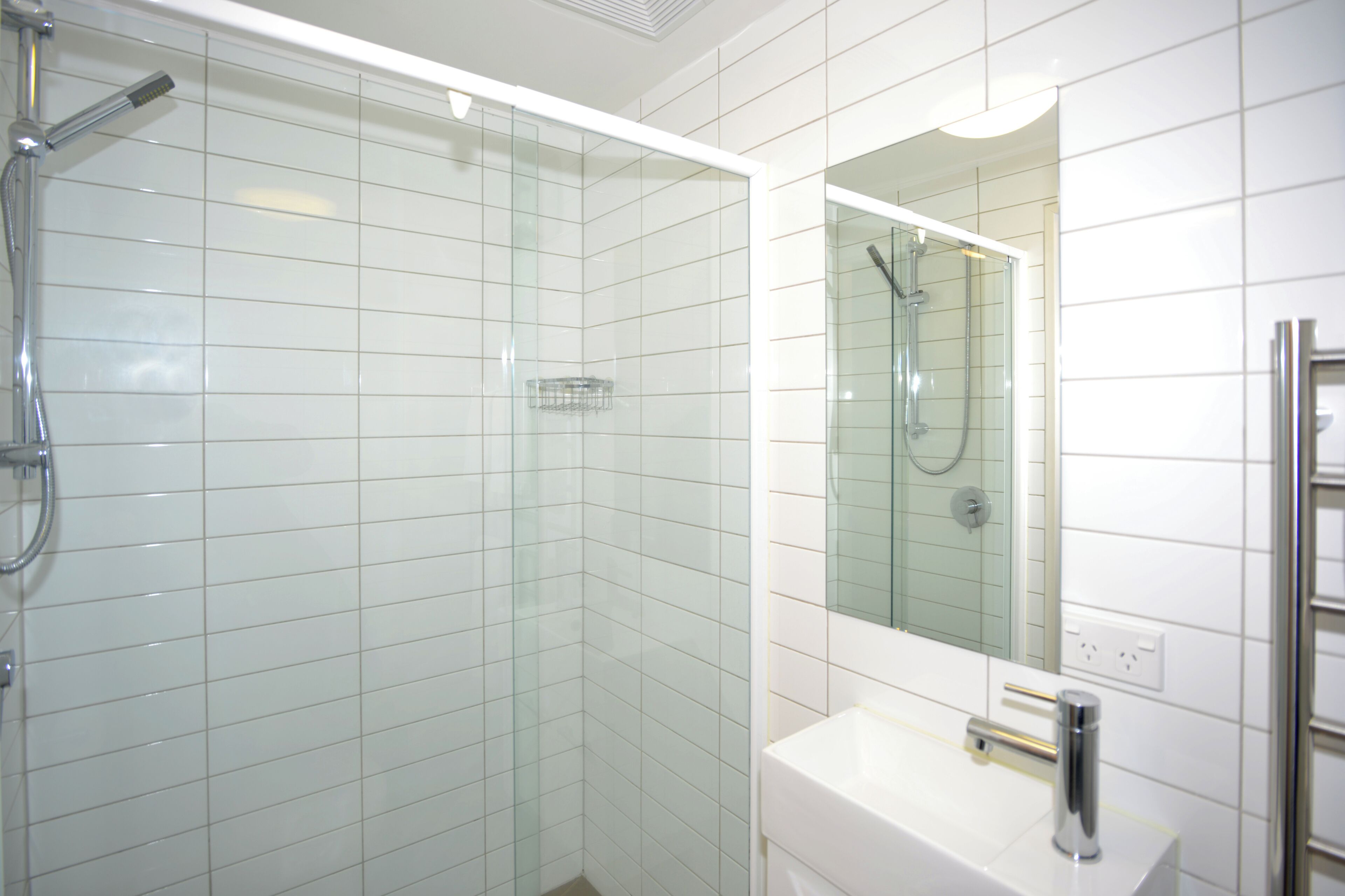 A modern bathroom with a glass-enclosed shower, a white sink, and a mirror above the sink.