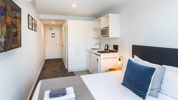 Una habitación de hotel con una cama, una kitchenette pequeña y una puerta que da a un baño.