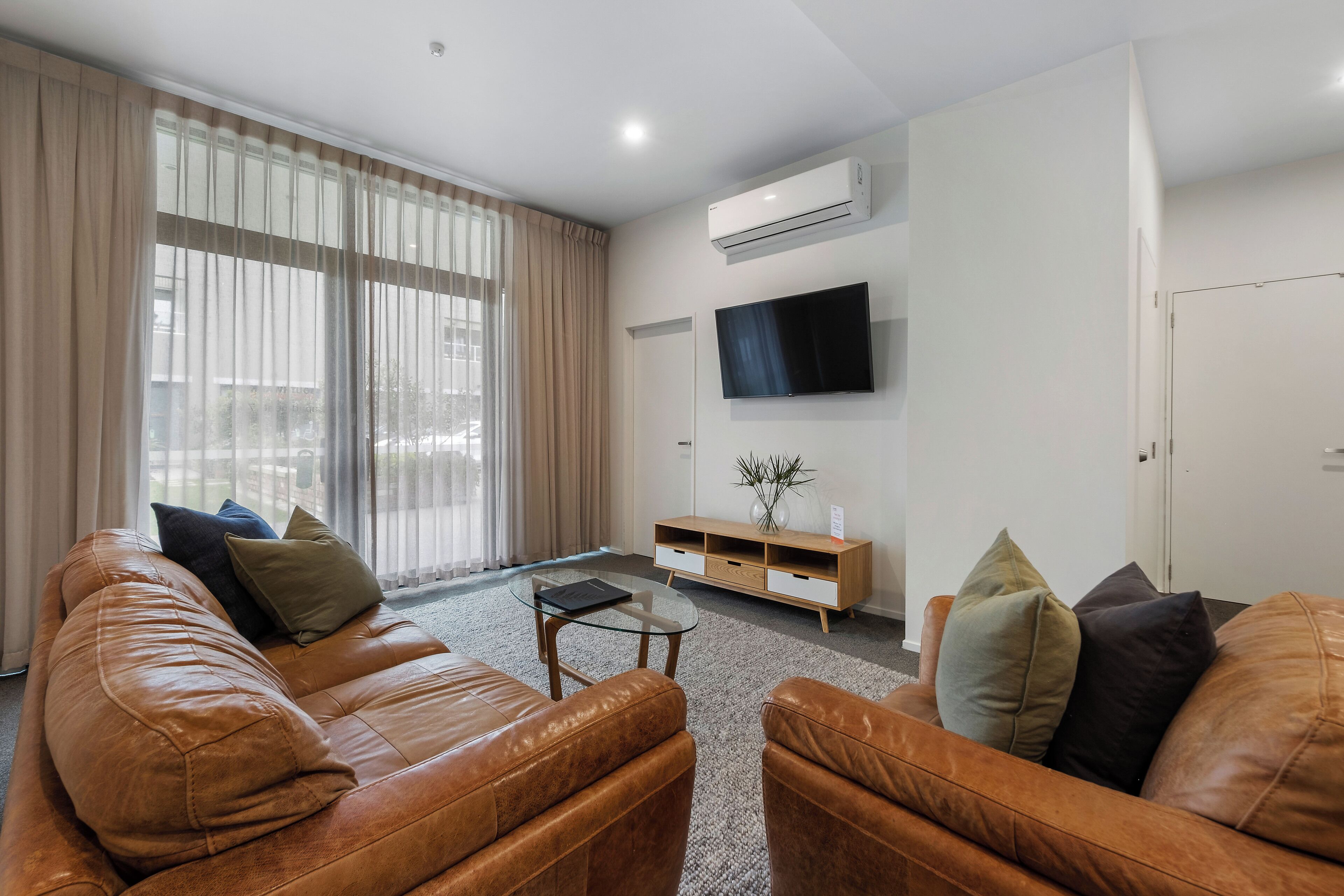 A modern living room with leather sofas, a glass coffee table, a flat-screen TV, and a wooden TV stand.