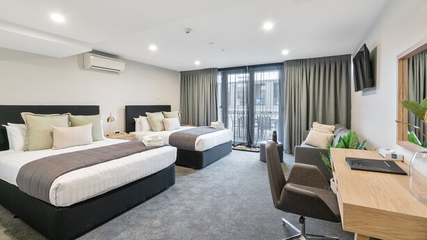 Habitación de hotel con dos camas, un escritorio, una silla, un televisor y un ventanal con cortinas.