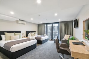 A hotel room with two beds, a desk, a chair, a TV, and a large window with curtains.