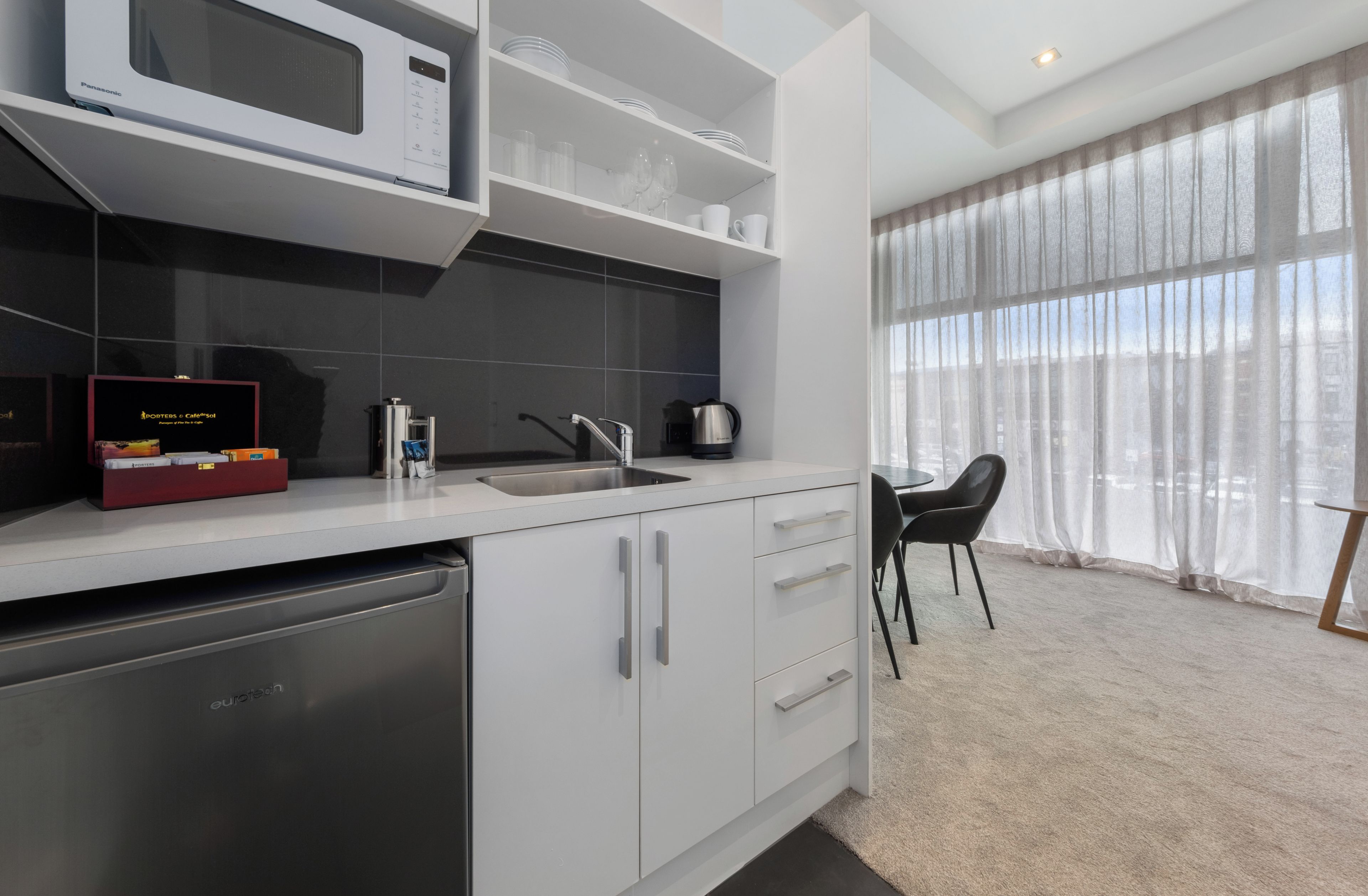 Una cocina moderna con lavavajillas, microondas y hervidor. Hay un comedor con mesa y sillas.