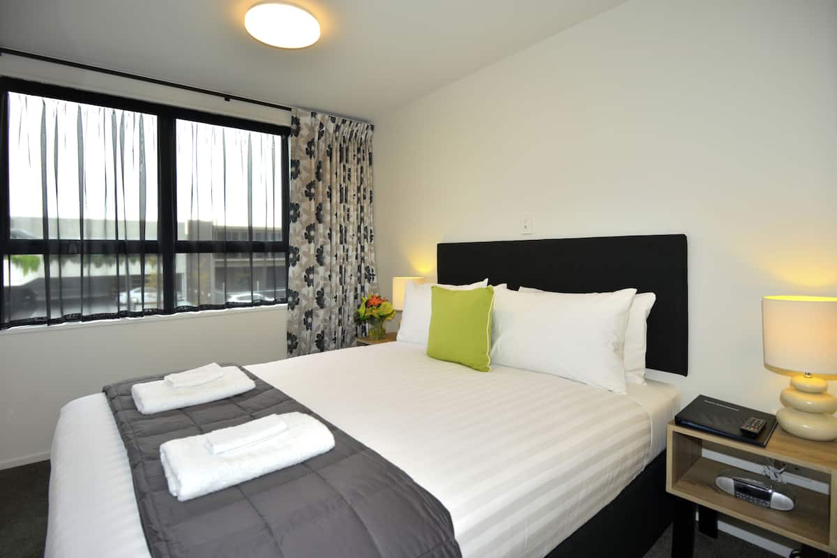 Une chambre d’hôtel avec un grand lit, une table de chevet avec une lampe et une fenêtre avec des rideaux.