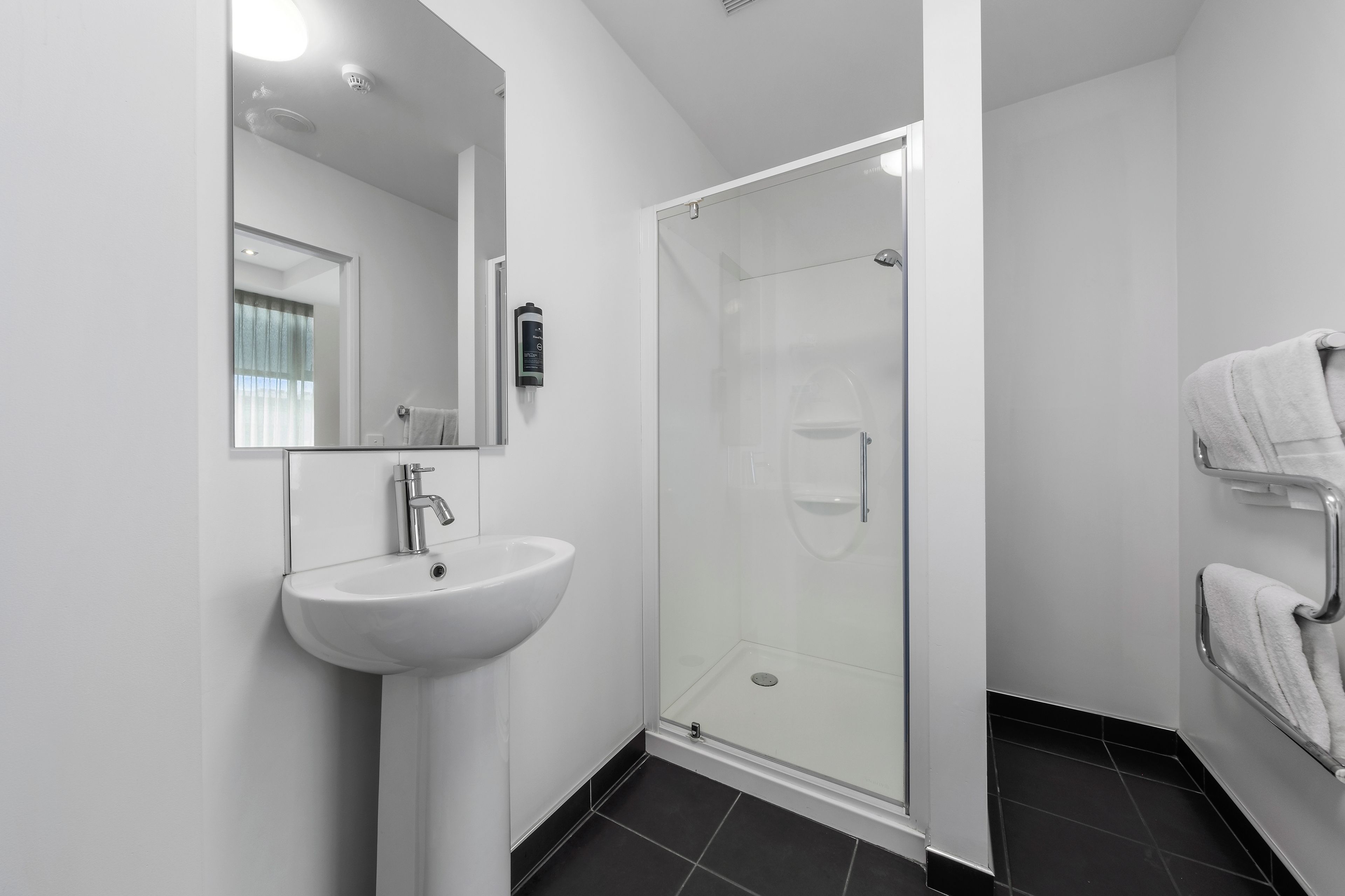 A modern bathroom with a white sink, a glass shower enclosure, and a towel rack.
