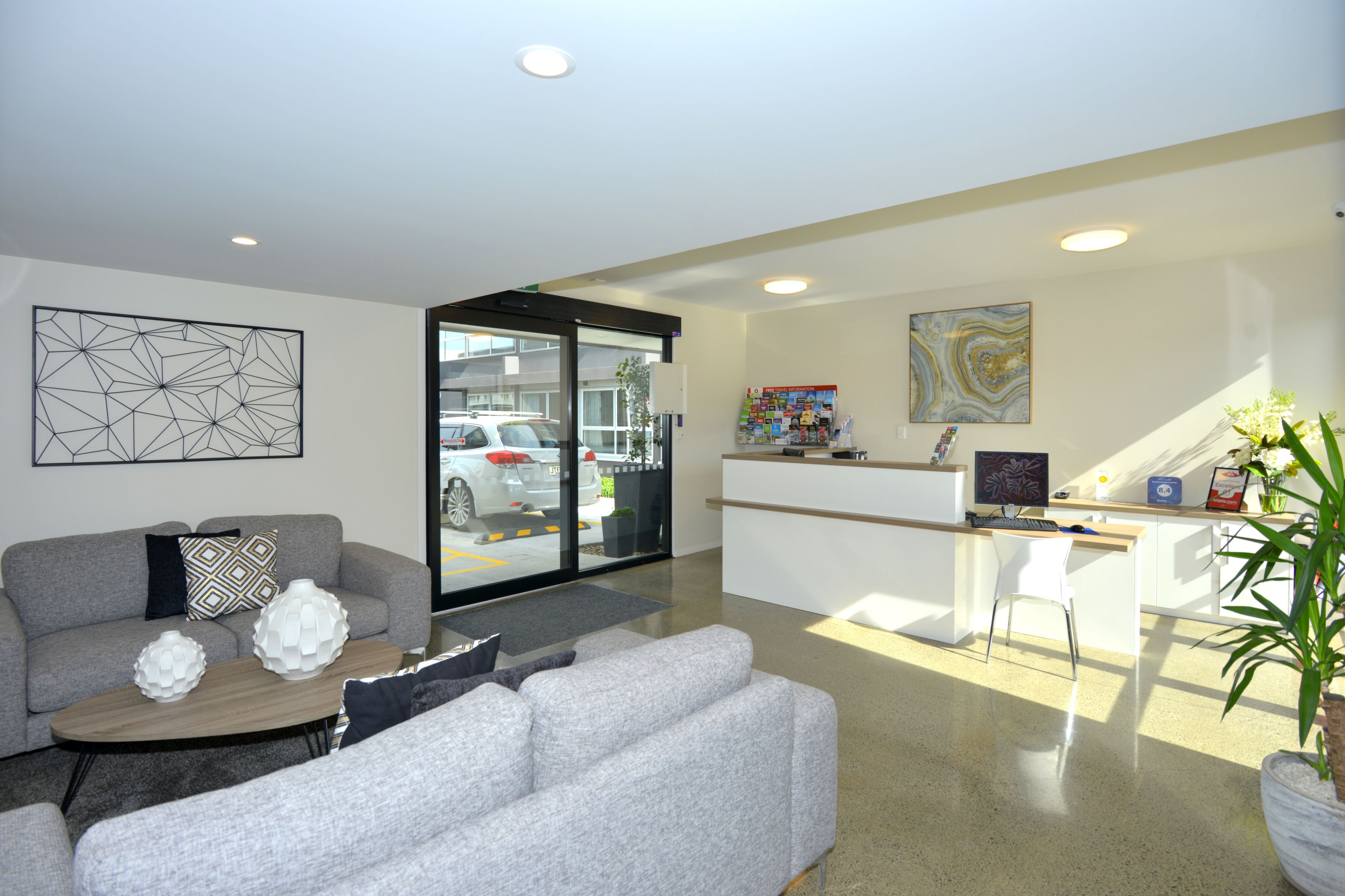A modern living room with a grey sofa, a coffee table, and a desk area with a computer and chair.