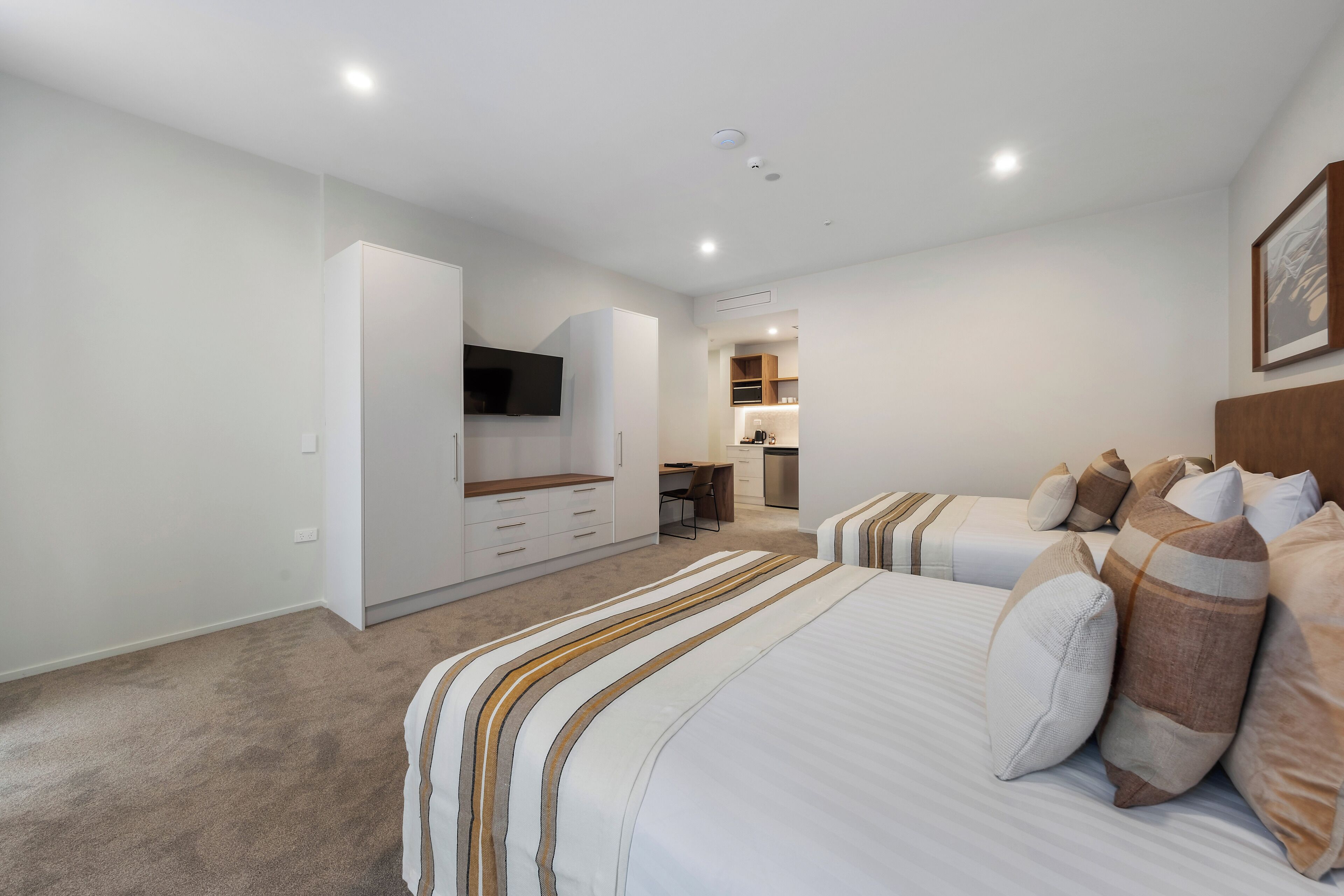 Quarto de hotel moderno com uma cama grande, uma escrivaninha e uma cozinha compacta.