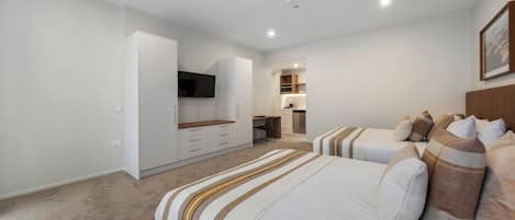 A modern hotel room with a large bed, a desk, and a kitchenette.