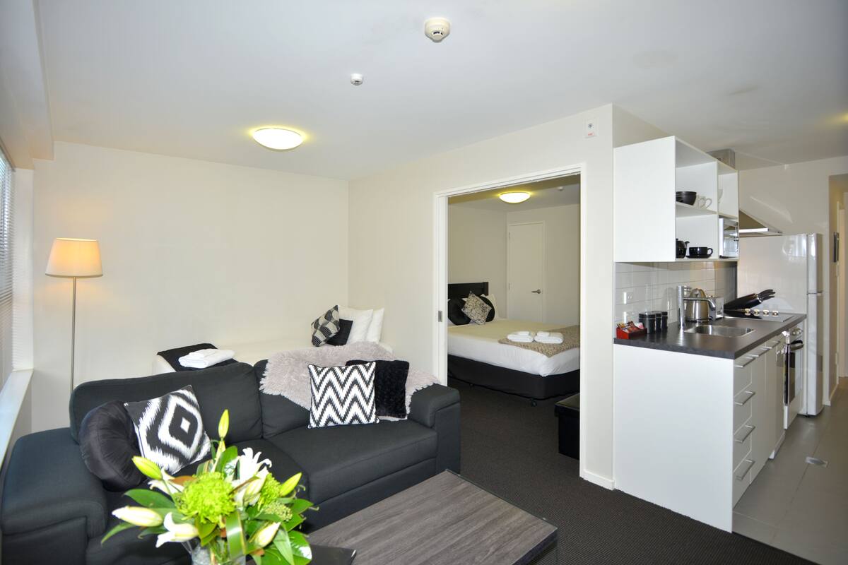Un espace de vie compact comprenant un canapé, une petite table basse, un lit et une kitchenette.
