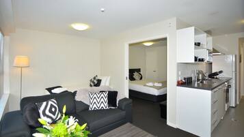 Un espacio habitable compacto con sofá, una mesita de centro, cama y kitchenette.