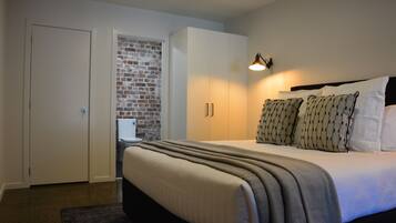 Un dormitorio con cama, mesita de noche, lámpara, armario y pared de ladrillo.
