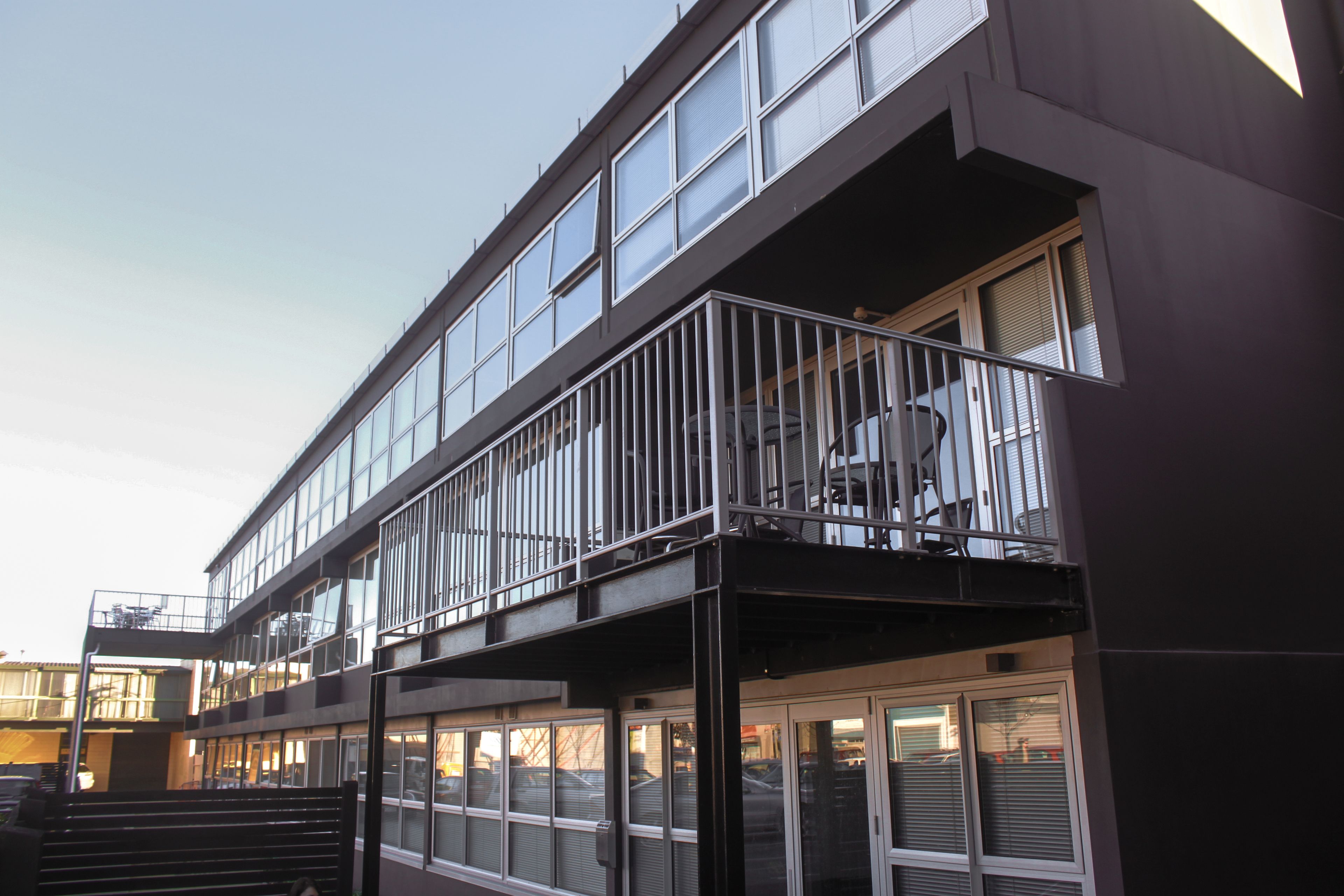 Un edificio moderno con fachada de vidrio, un balcón con barandillas metálicas y una escalera que conduce a la entrada.