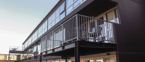 Un edificio moderno con fachada de vidrio, un balcón con barandillas metálicas y una escalera que conduce a la entrada.