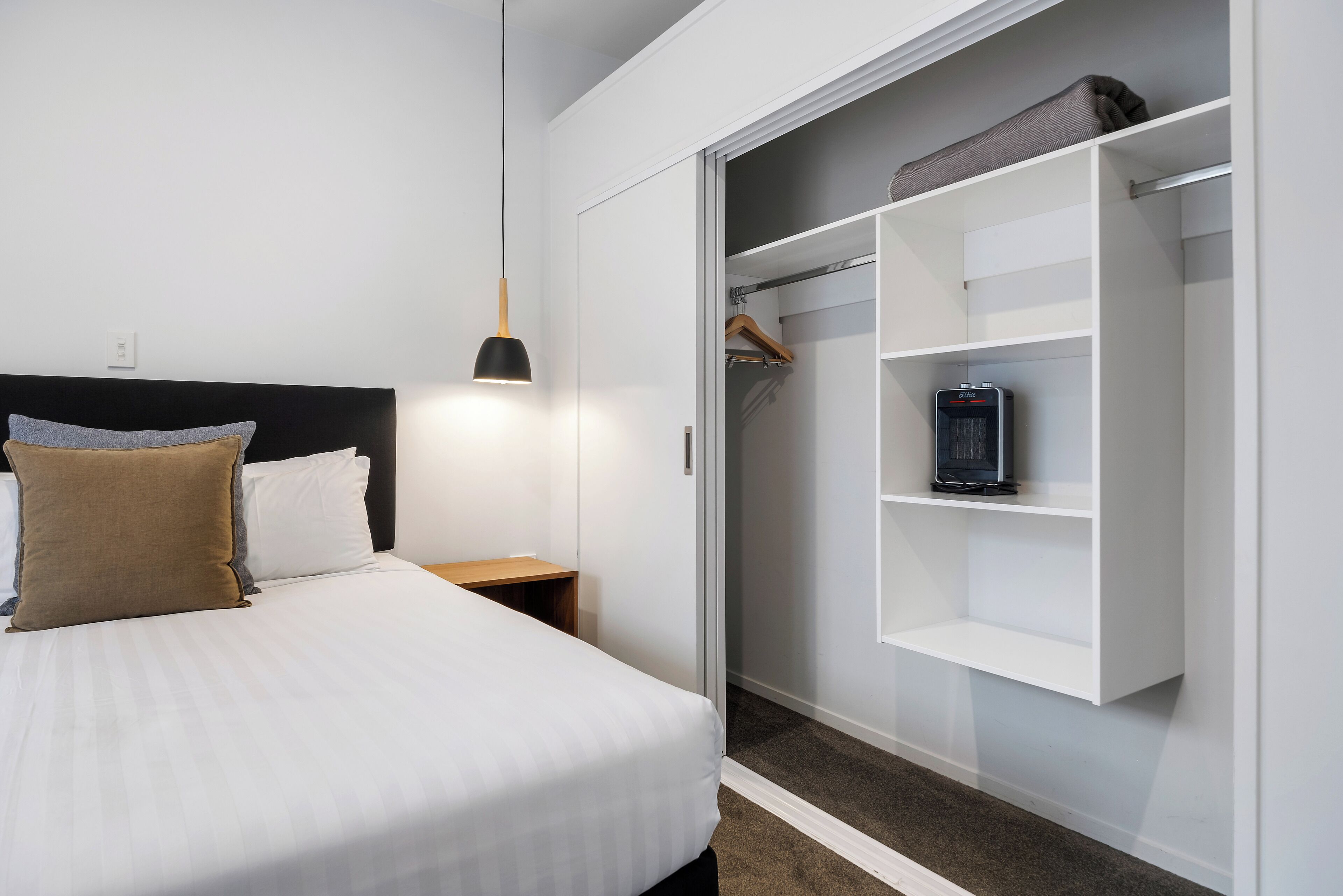 Un dormitorio ordenado con cama, mesita de noche y vestidor con estantes.