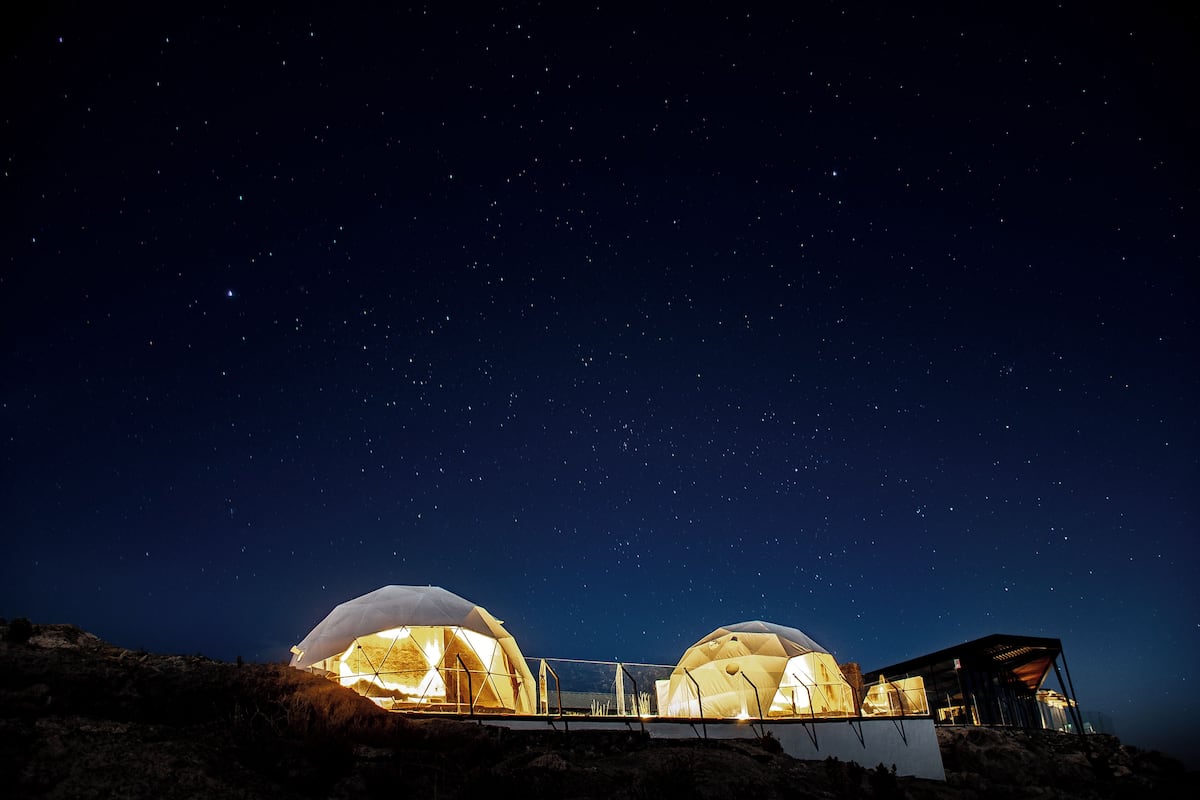 Duas estruturas em forma de cúpula com interiores iluminados, ao pôr do sol sob um céu estrelado.