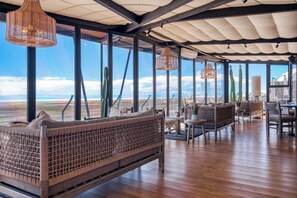 Amplio espacio interior con vistas al paisaje desértico, con mobiliario de mimbre e iluminación colgante.
