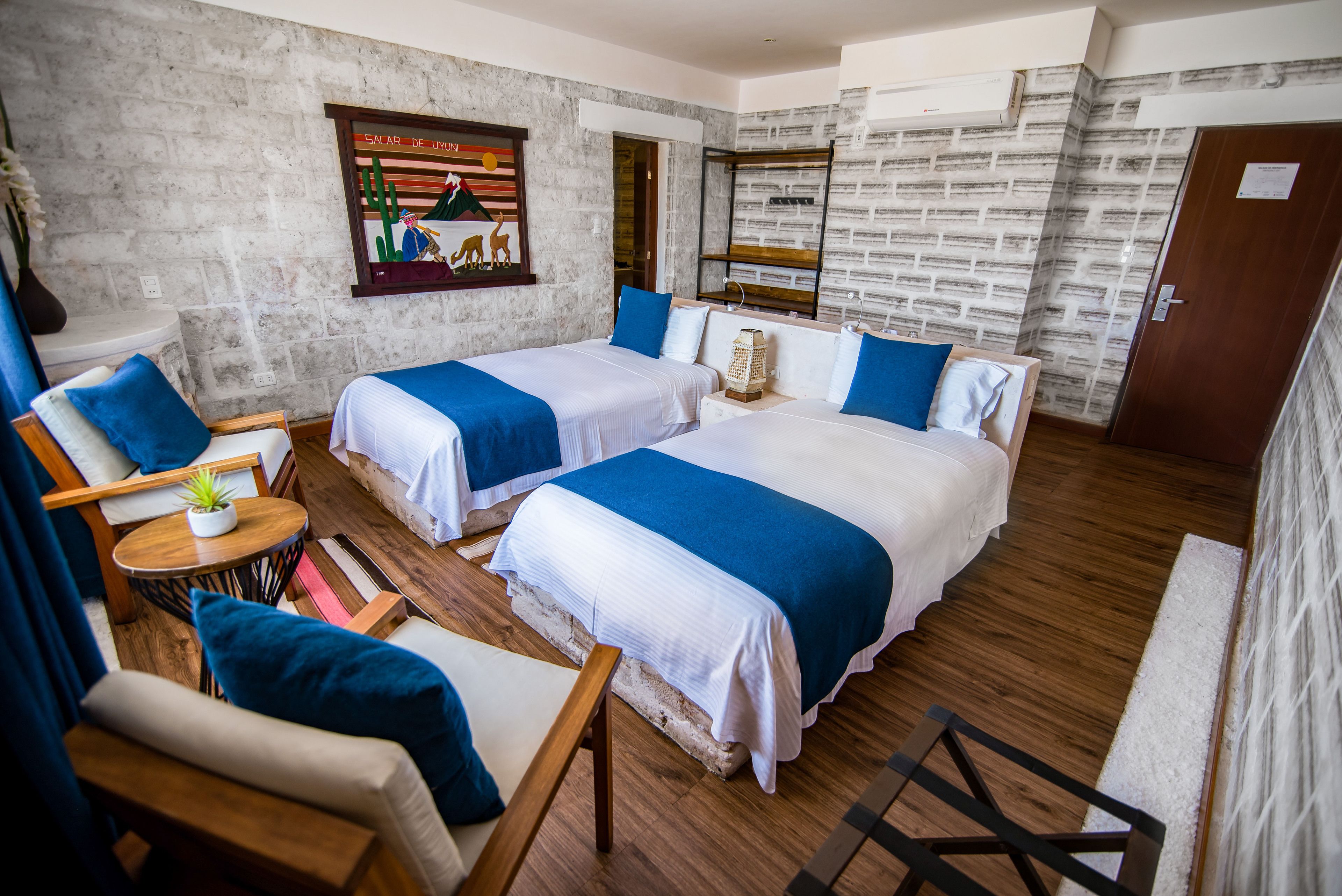 A hotel room with two beds, a small round table with a plant, a sofa, and a wooden floor.