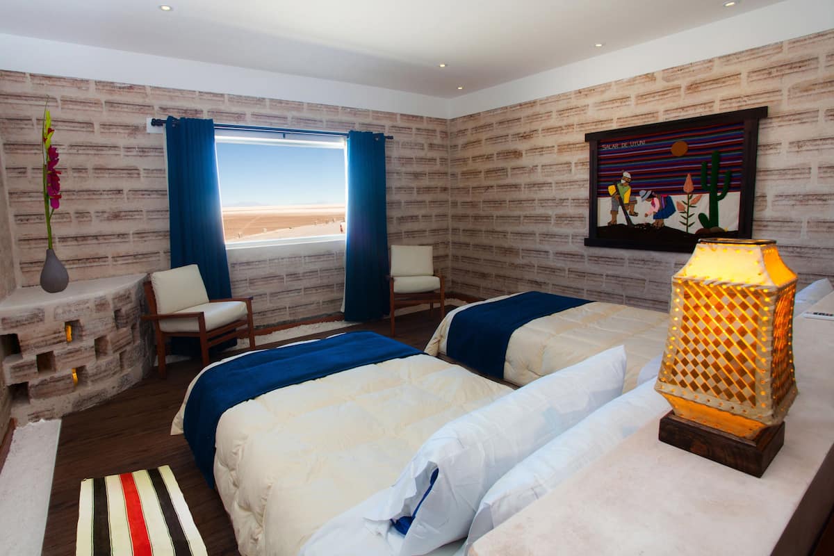 Quarto com duas camas, janela com vista, parede de tijolos e um quadro.