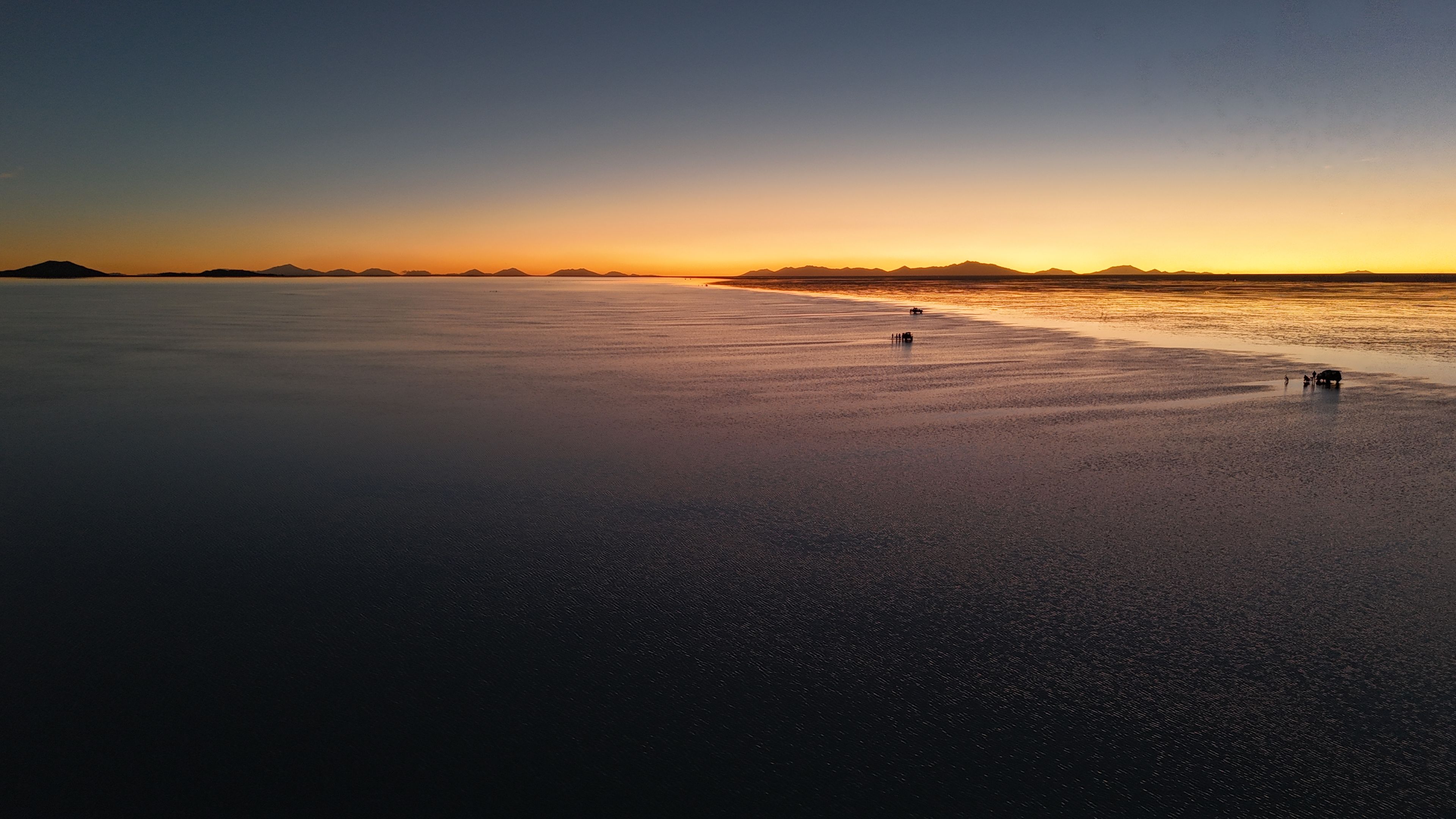 A vast, flat landscape with a calm body of water and distant mountains during sunset.