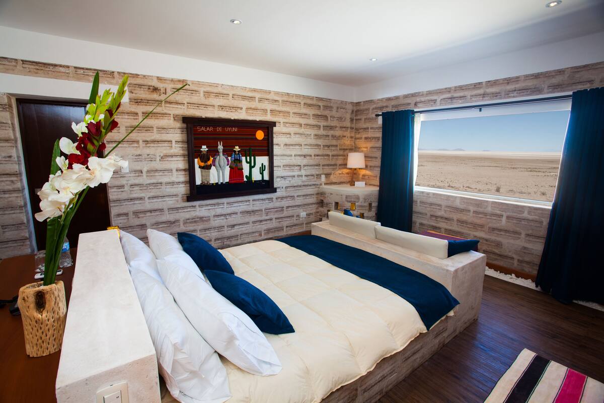 Quarto com uma cama grande, vista para o deserto e um mural na parede.