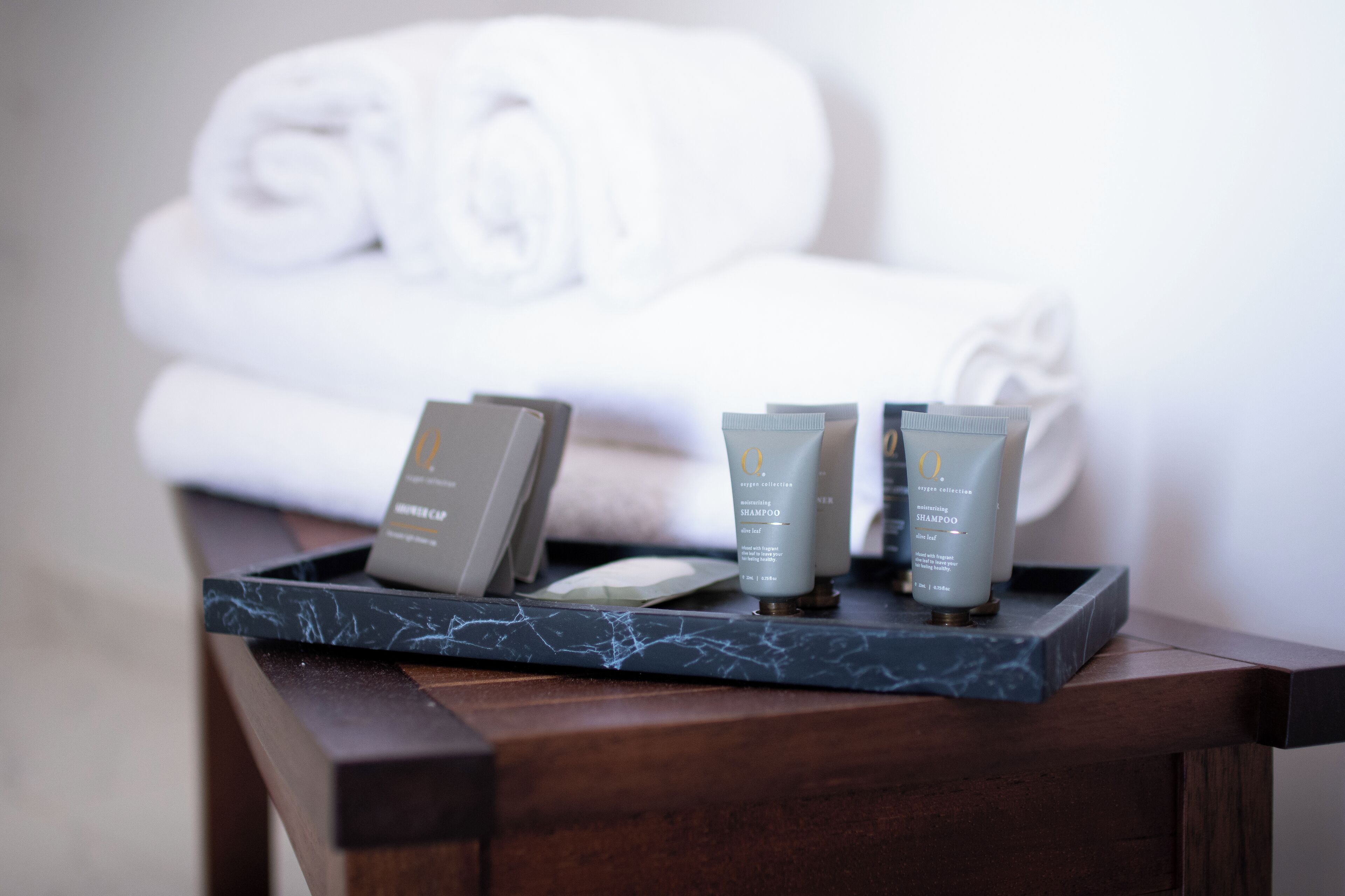 A tray with toiletries on a wooden table, with towels in the background.