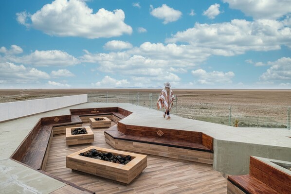 Amplia terraza al aire libre con macetas de madera y zonas de estar, con vistas panorámicas del paisaje.