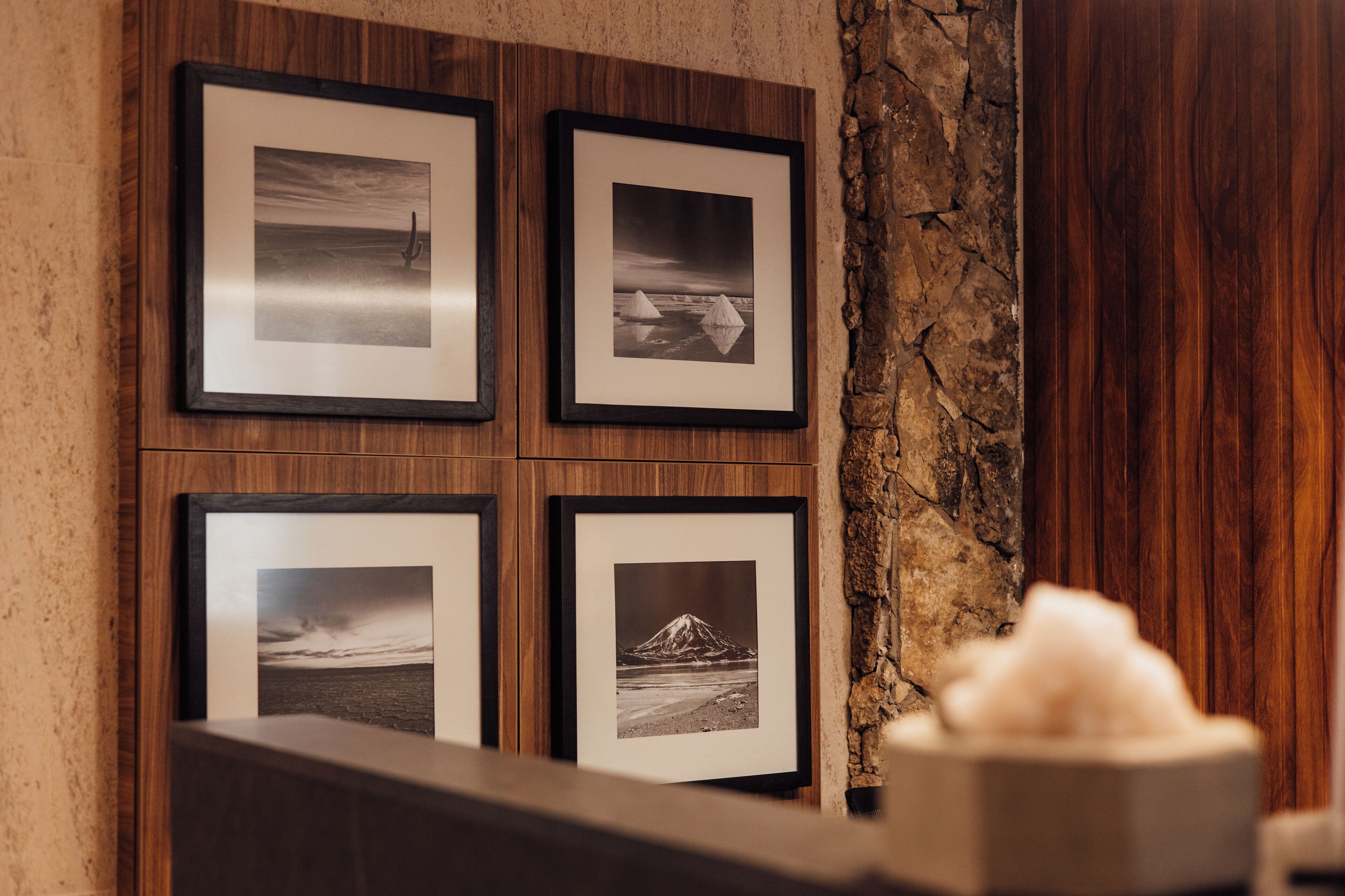 En vägg med fyra inramade svartvita fotografier av landskap, en stenmur och en träpanel.