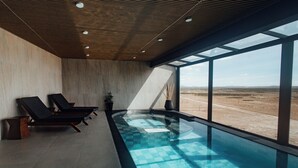 A modern indoor pool area with two lounge chairs and a large window overlooking a desert landscape.