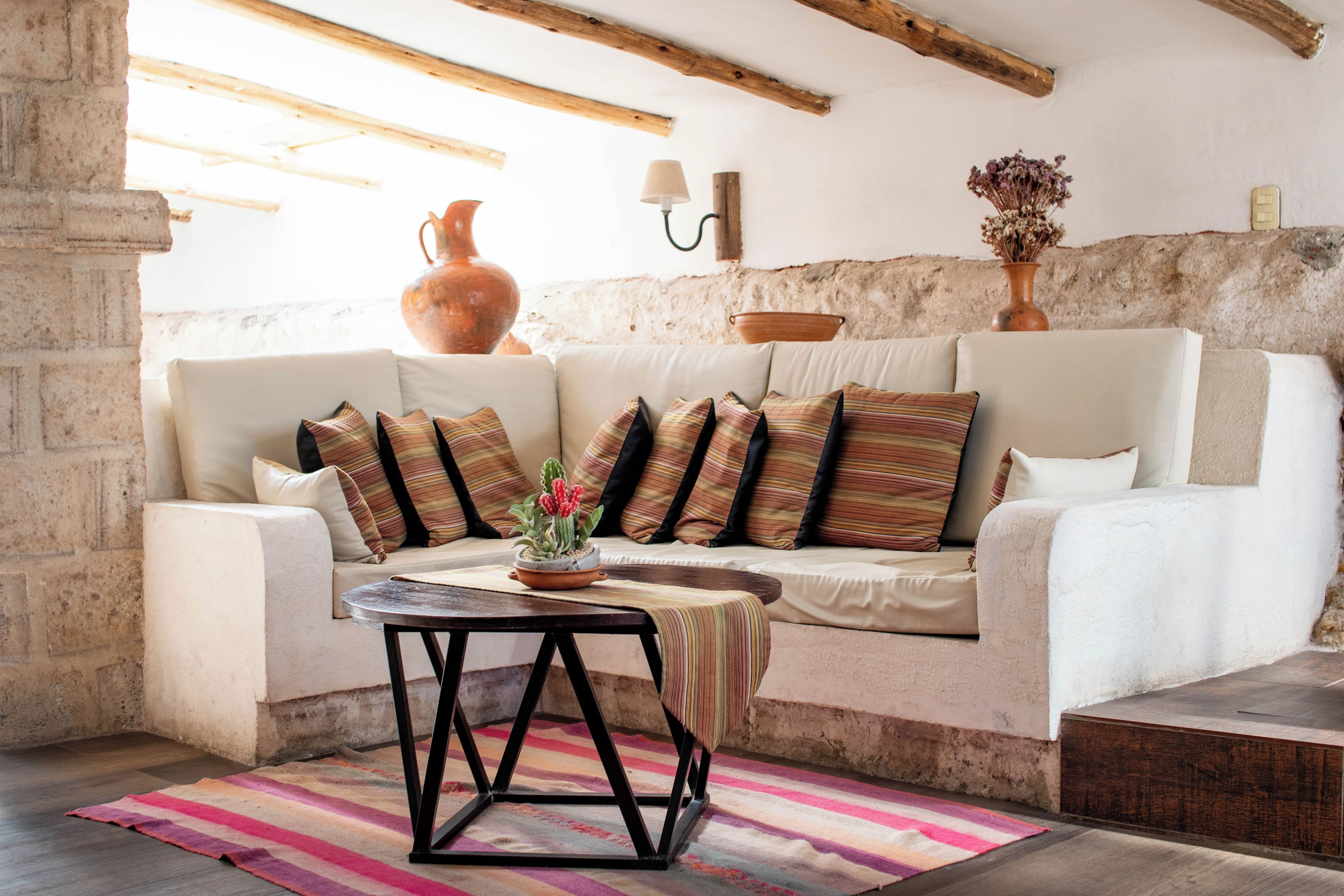 A cozy living room with a white sofa, striped cushions, a small table, and a colorful rug.