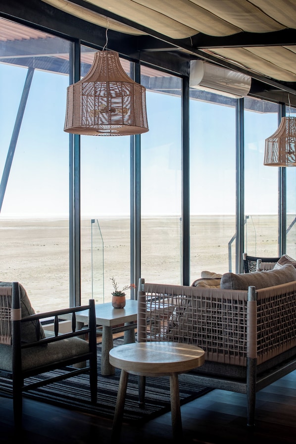 Ein Zimmer mit großen Fenstern, Korbmöbeln und Blick auf den Strand.