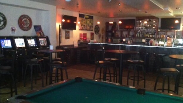 Zona de bar con mesas de billar, barra y varios adornos en las paredes.