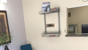 Una habitación con una mesa redonda, una silla azul, un estante con objetos y un espejo en la pared.
