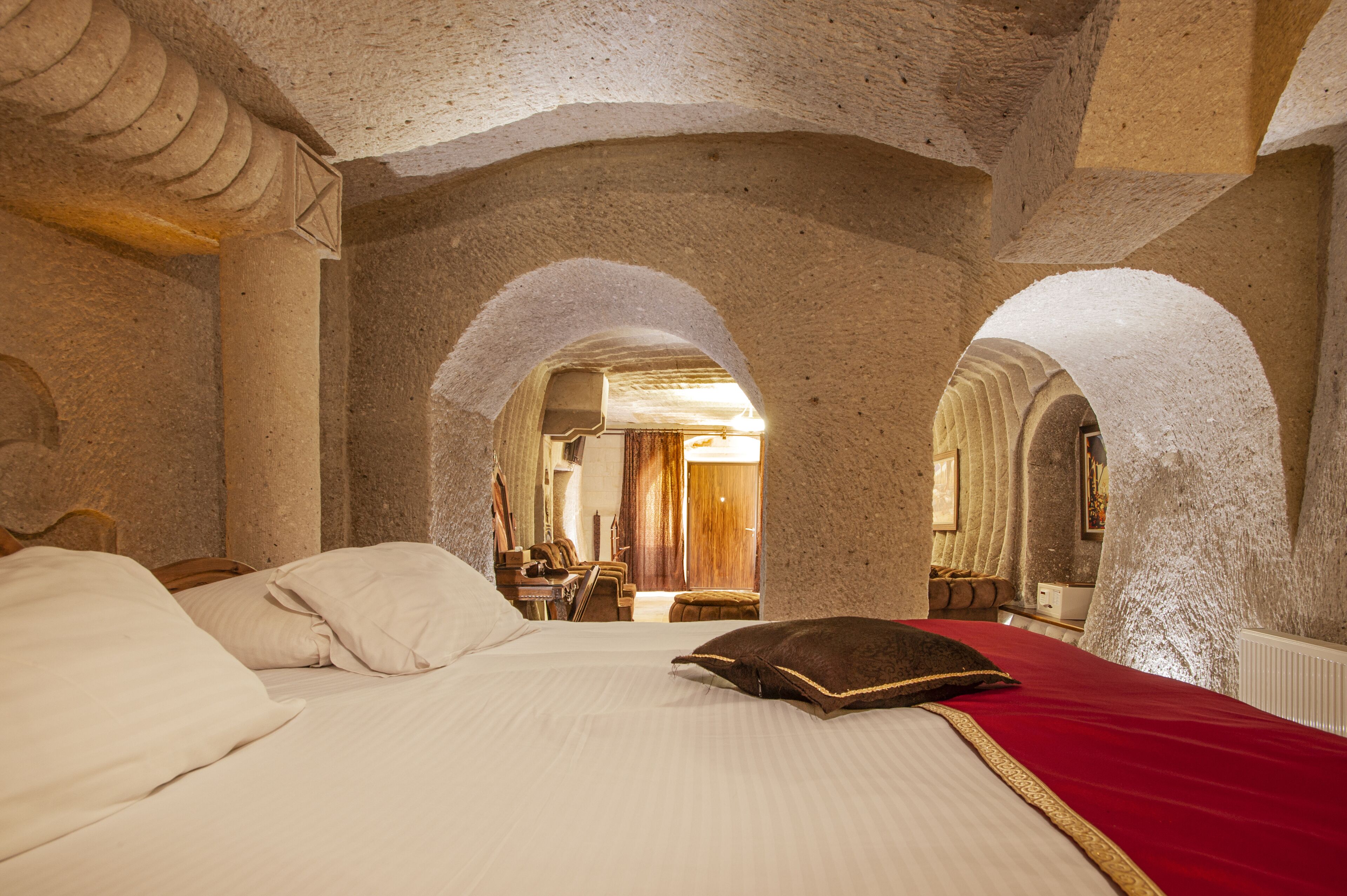 A room with a large bed, stone arches, and a view into another room.