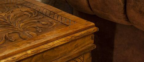 A wooden chest with intricate carvings, positioned next to a brown upholstered chair.