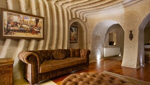 A room with a vintage sofa, a patterned rug, and a painting on the wall. - Ottoman Cave Suites (Nevsehir)