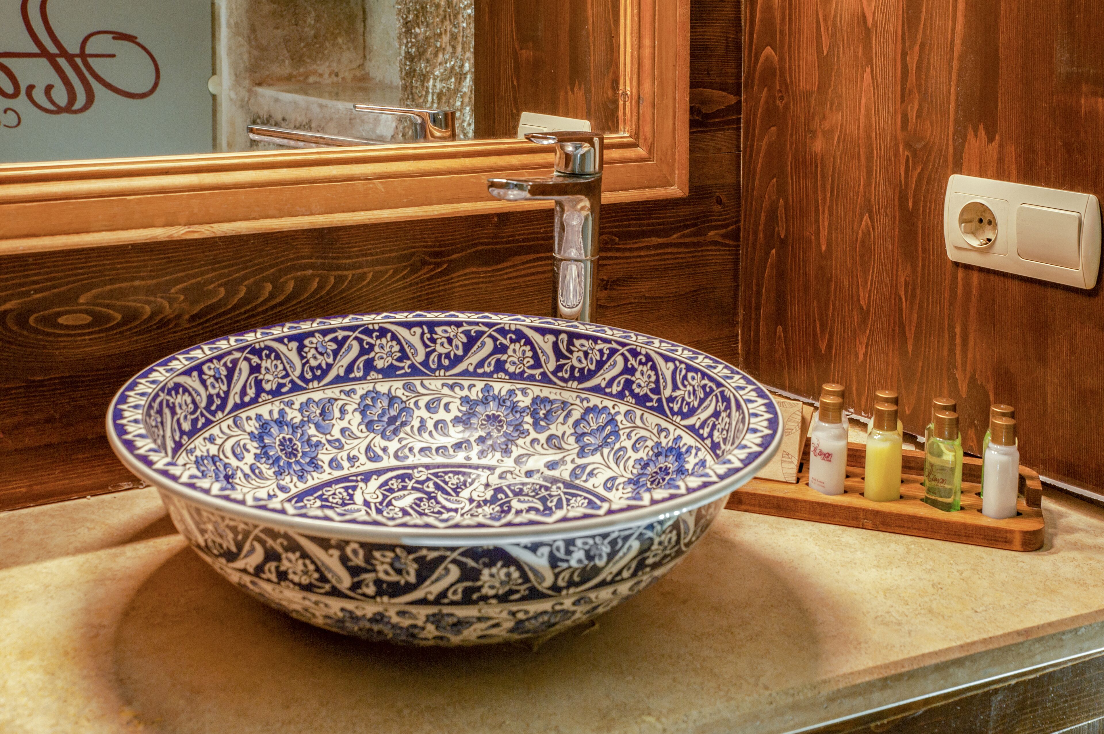 A bathroom with a large blue and white patterned bowl sink, a wooden vanity, and a mirror above it.