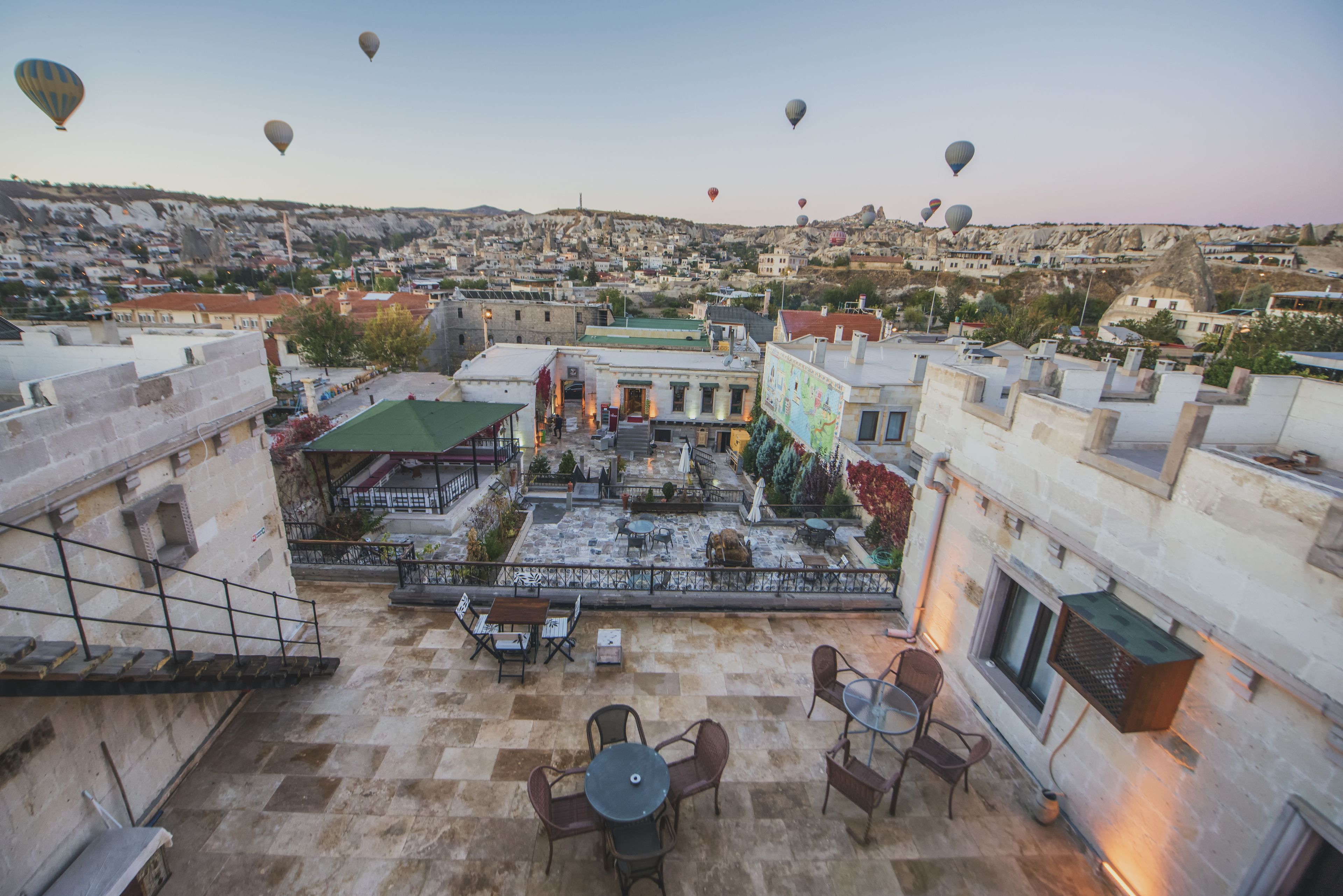 A rooftop terrace with outdoor seating, a view of the cityscape, and hot air balloons in the distance.