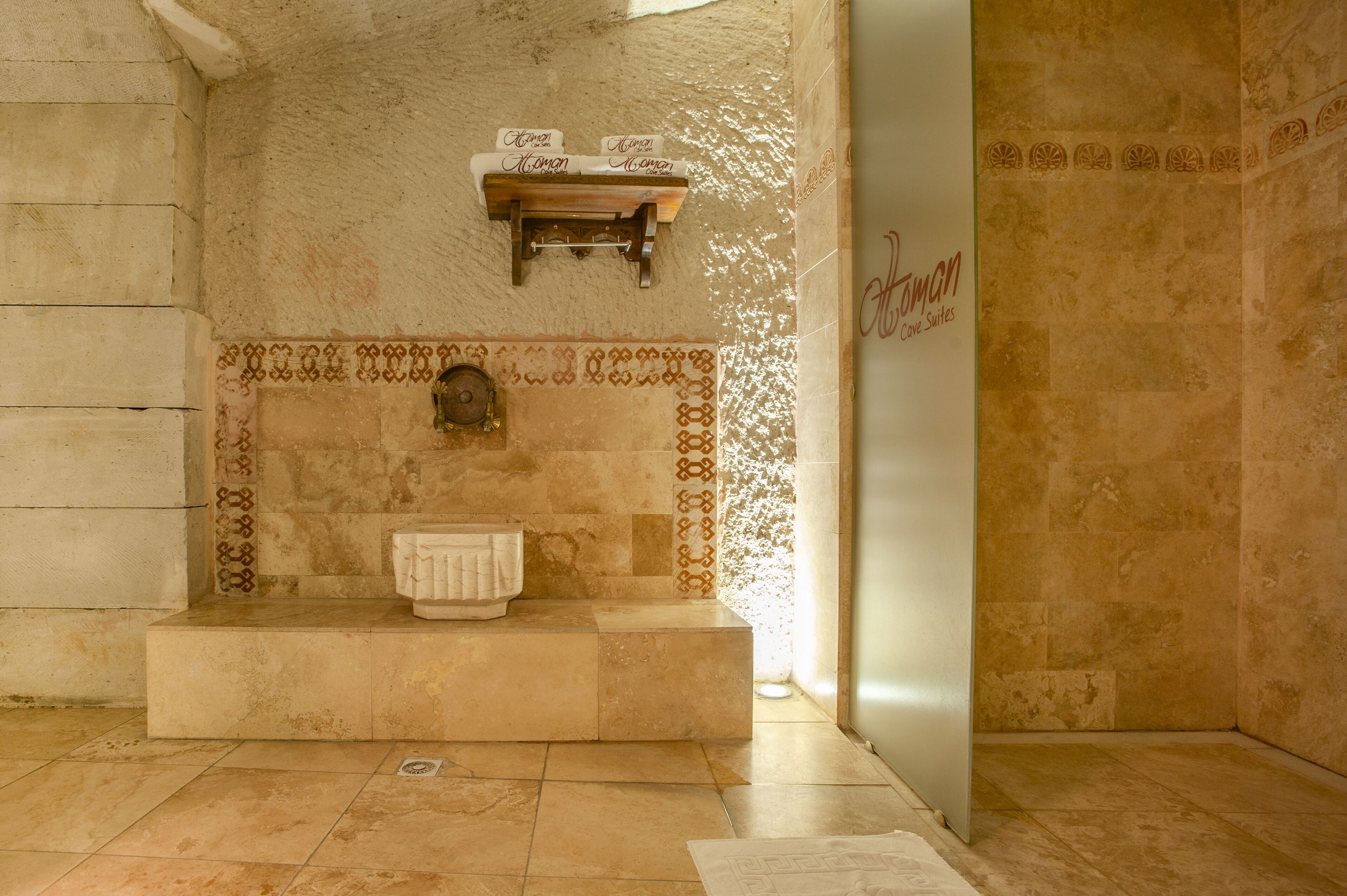 A bathroom with a stone wall, a wooden shelf with towels, and a sign that reads "Atonan Cove Suites."