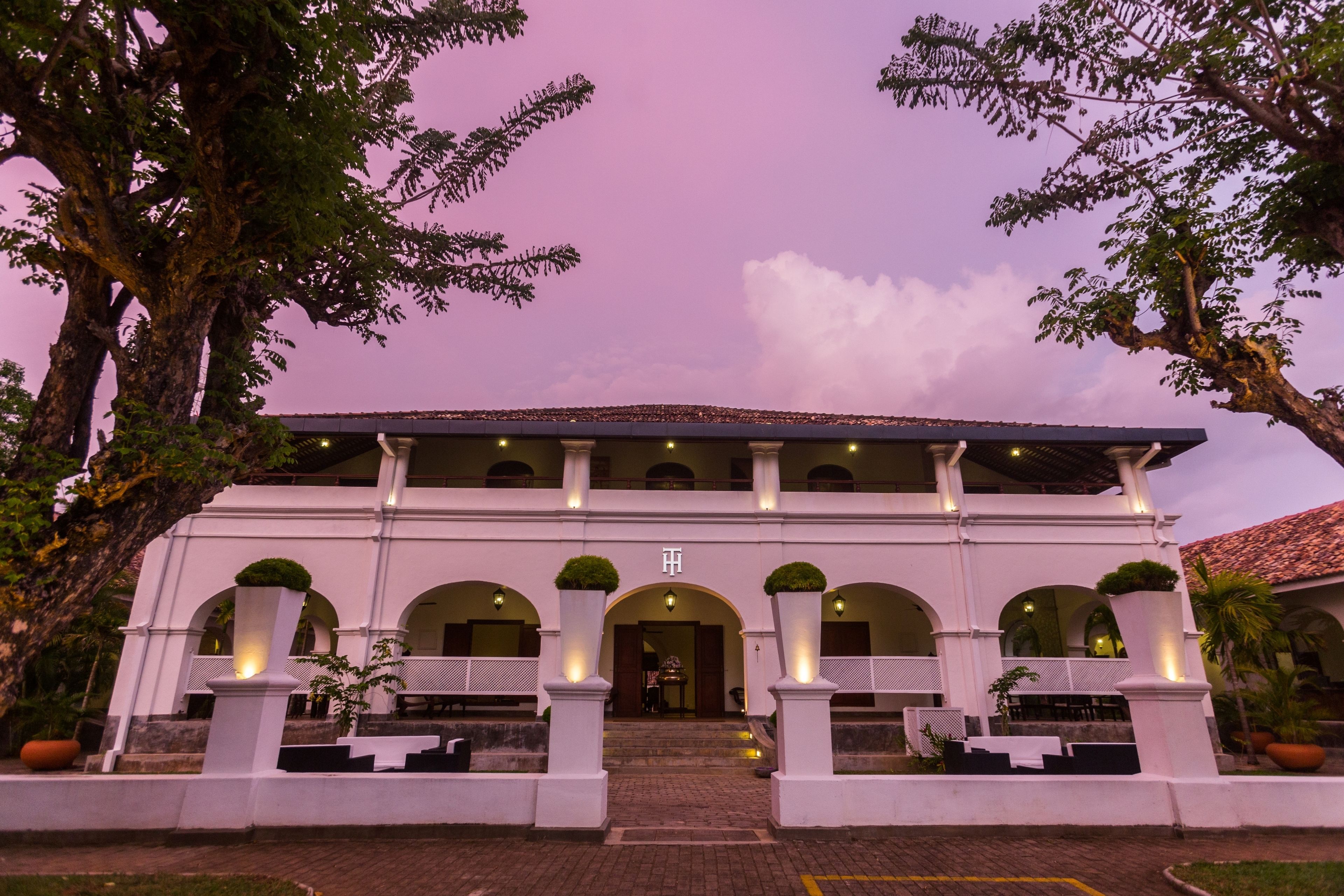 A white building with multiple arches and columns, a covered entrance, and potted plants.