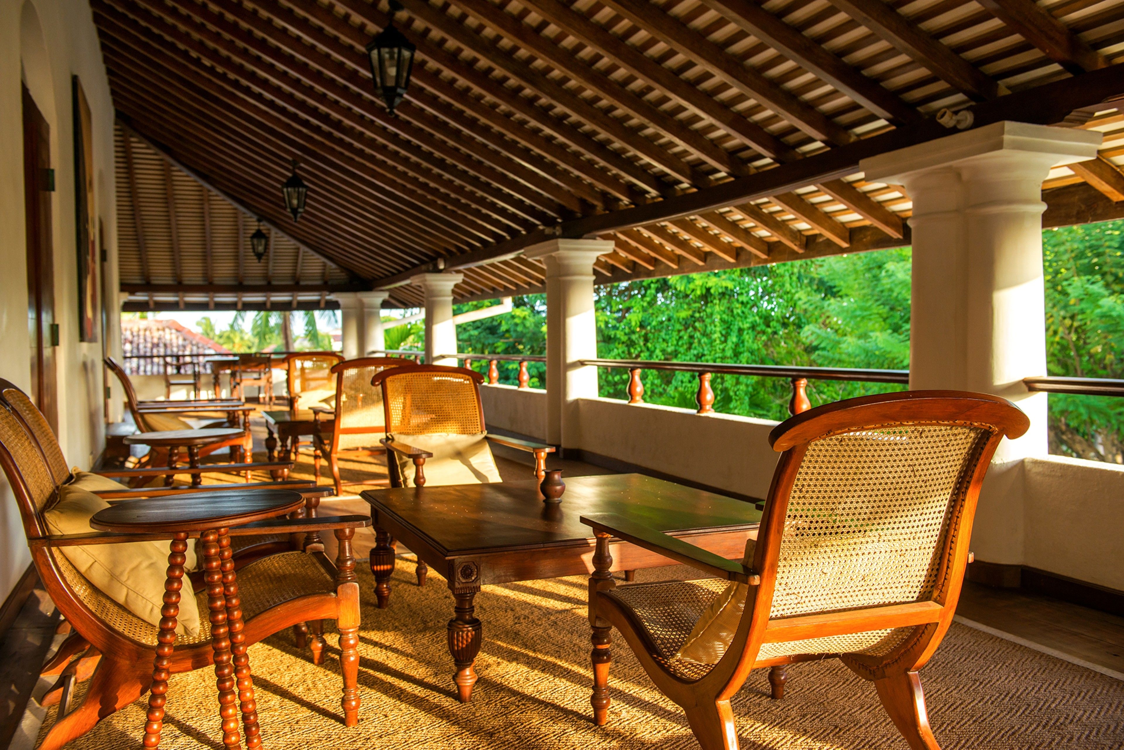 A covered outdoor seating area with wooden furniture and a view of greenery.