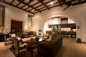 A spacious living room with a high ceiling, wooden beams, and a large arched doorway leading to another room. There are multiple seating areas with sofas and chairs, and a coffee table in the center. - Tamarind Hill by Asia Leisure (Galle)