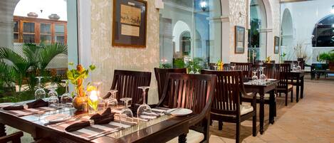 A dining area with wooden tables and chairs, glassware, and a floral centerpiece.