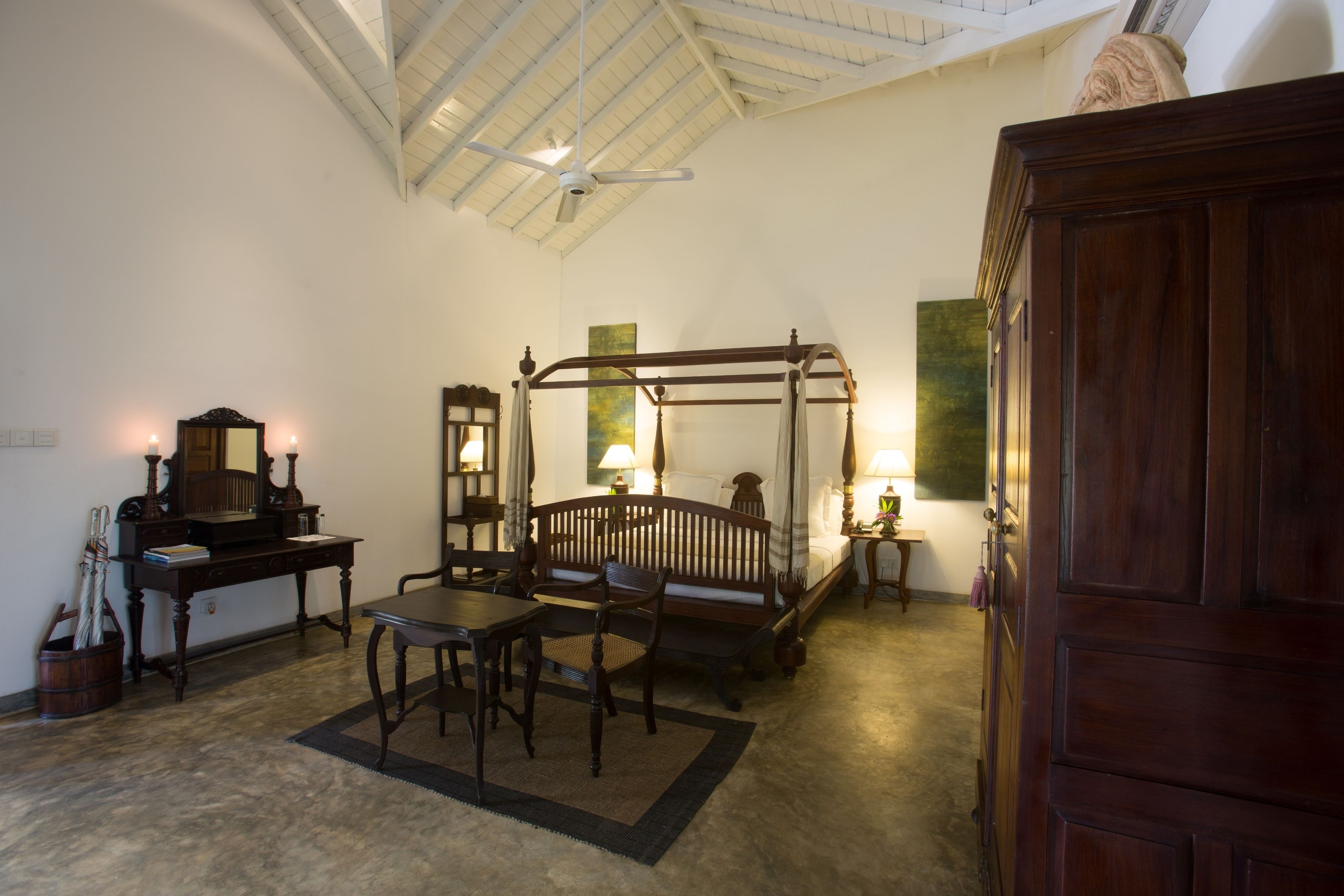 A traditional bedroom with a four-poster bed, a desk with a mirror, and a wooden wardrobe.