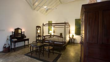 A traditional bedroom with a four-poster bed, a desk with a mirror, and a wooden wardrobe.