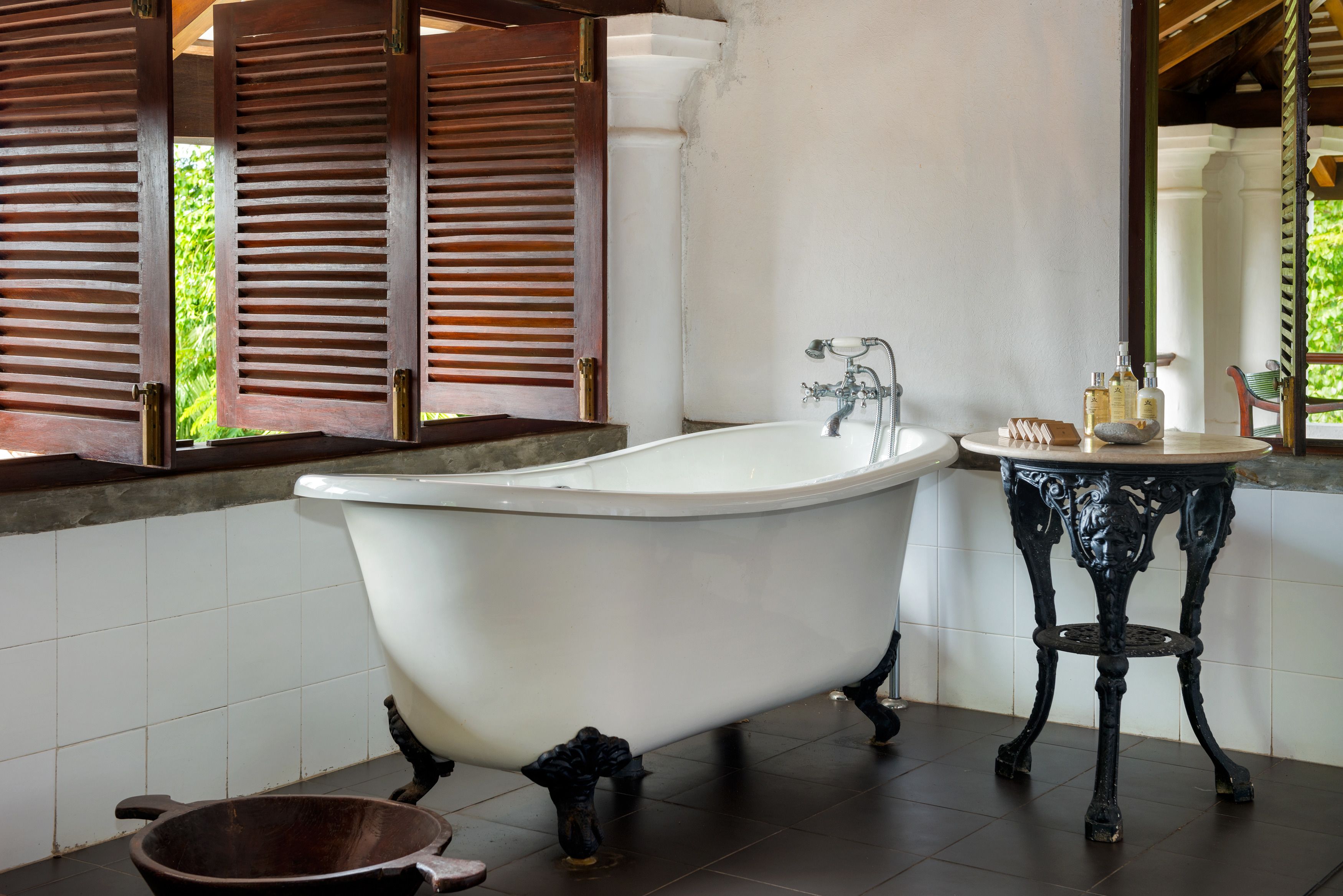 A bathroom with a freestanding bathtub, a sink with ornate legs, and a window with wooden shutters.